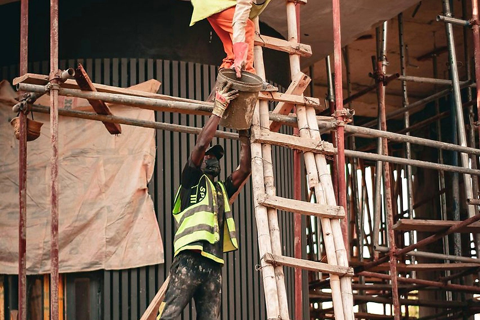 Free Two construction workers in safety gear collaborate on scaffolding at a building site. Stock Photo