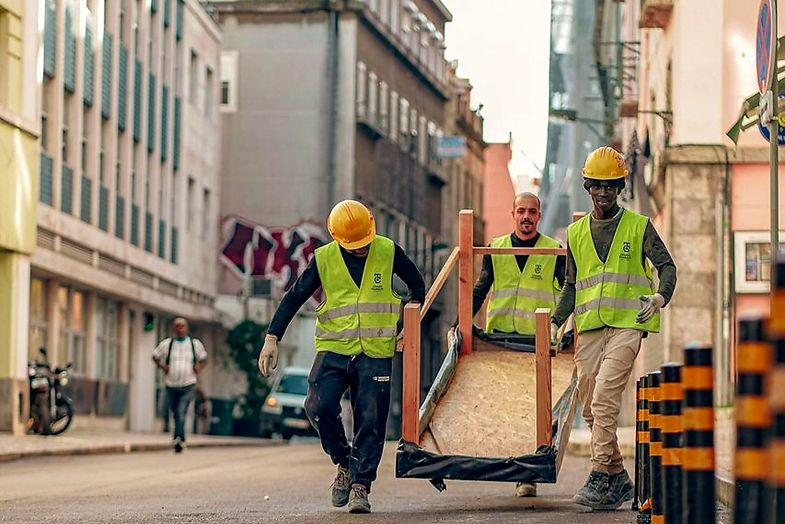 Free Three construction workers in safety vests transport heavy equipment on an urban street. Stock Photo